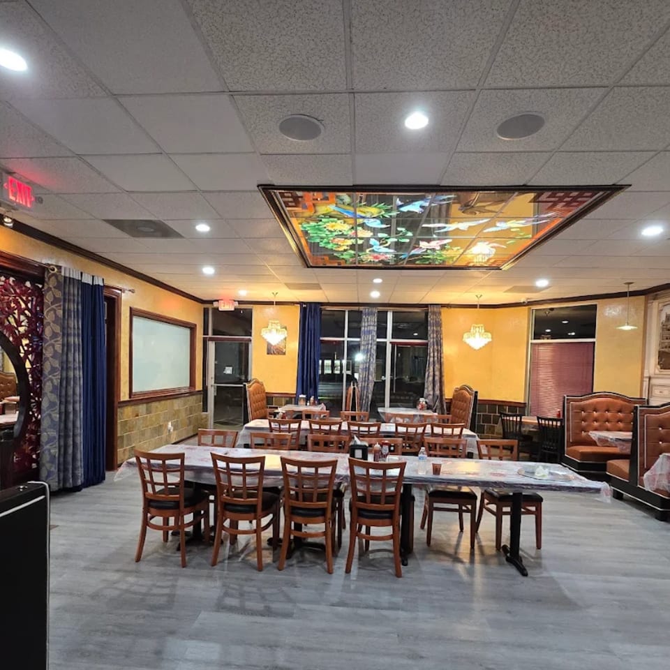 Spacious restaurant dining room with tables, booths, and a decorative stained-glass ceiling panel.