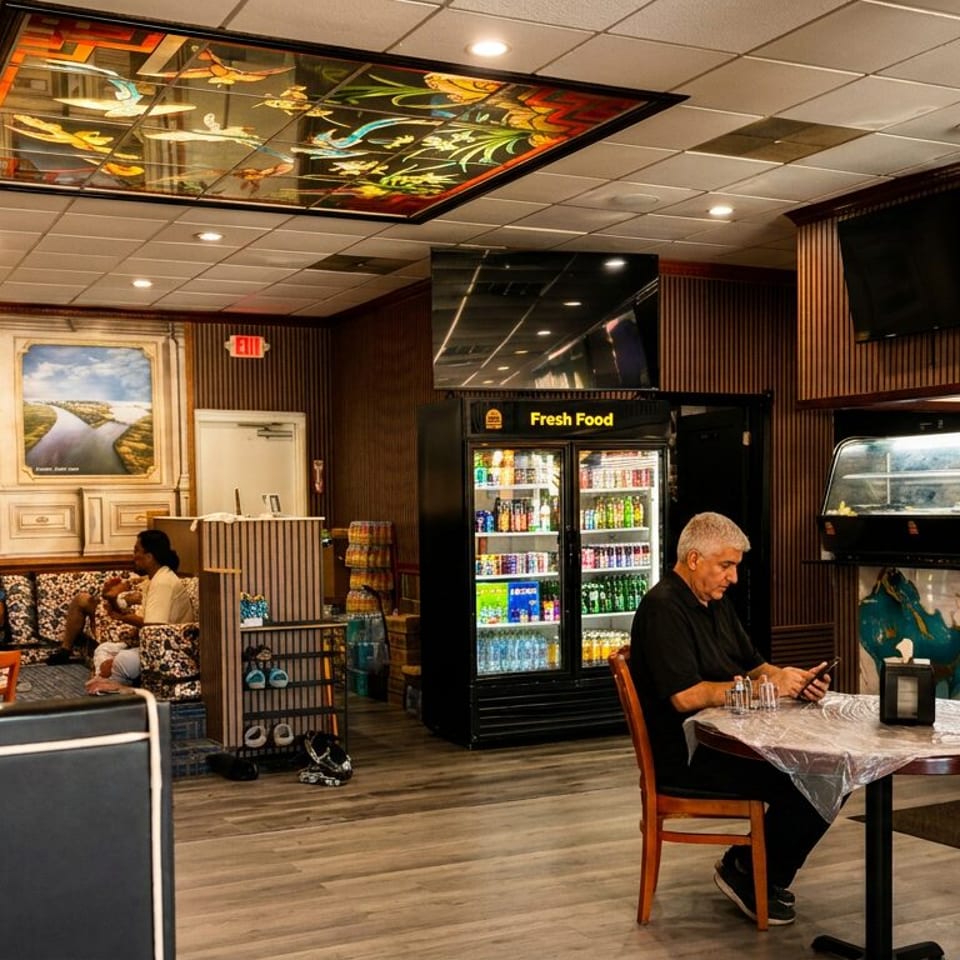 Casual restaurant interior with customers, booths, a drink fridge, and decorative ceiling art.
