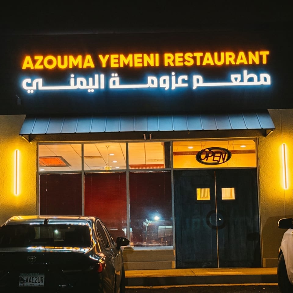 Azouma Yemeni Restaurant exterior at night with glowing neon signs and parked cars.