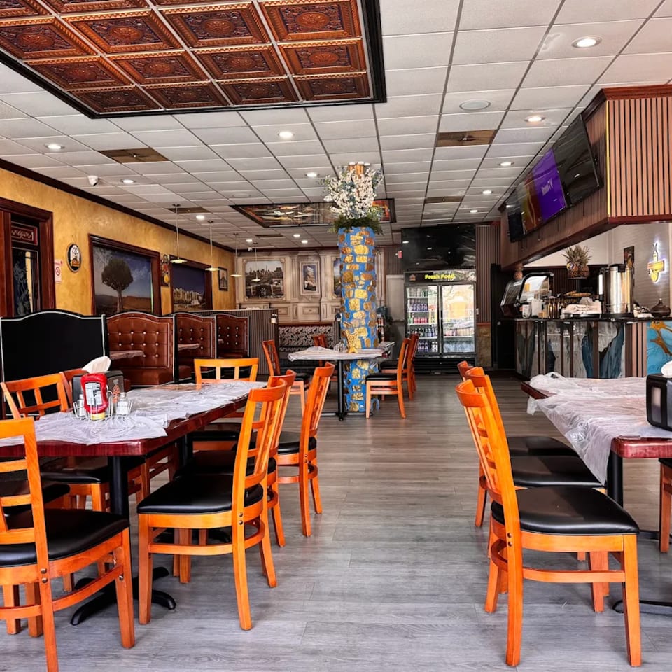 Spacious restaurant interior with orange chairs, wooden tables, and decorative ceiling tiles.