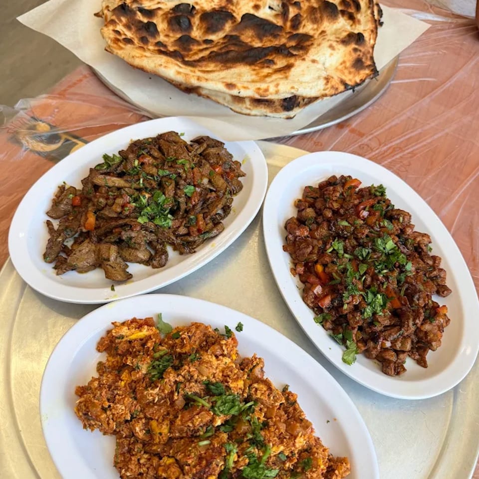 Three plates of savory meat dishes and a stack of charred flatbread on a metal tray.
