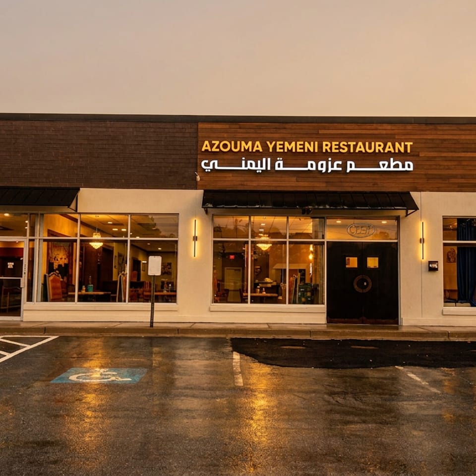 Exterior of Azouma Yemeni Restaurant at dusk, with illuminated sign, large windows, and wet parking lot.